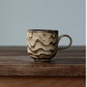 Wavy ceramic coffee mug with rustic brown flowing patterns on a wooden table