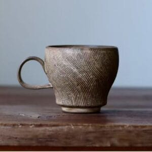 Profile view of an earth-toned wabi-sabi ceramic cup showing fine ribbed textures