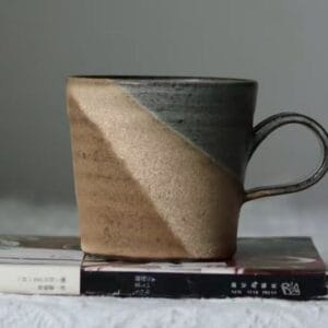 Two tone rustic ceramic mug with a dark and sandy glaze sitting on a book