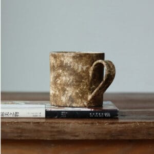 Wabi-Sabi style textured stoneware studio mug sitting on a book over a wooden table