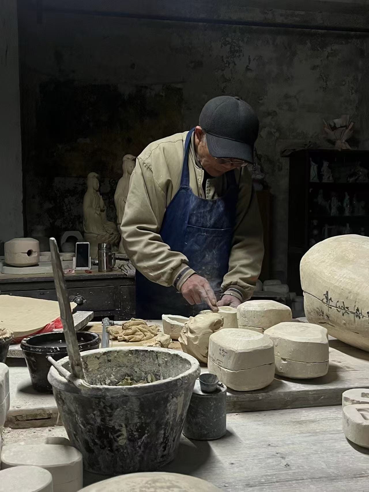 An elderly ceramic artisan master meticulously working with clay molds in a traditional Jingdezhen porcelain workshop.