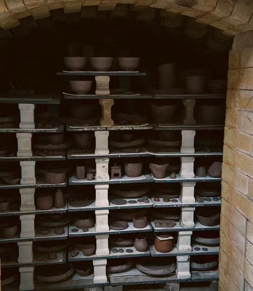 Unfired ceramic pots and bowls carefully stacked inside a traditional brick kiln in Jingdezhen, ready for high-temperature firing.