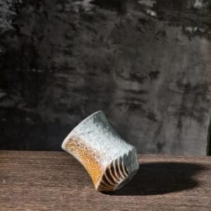 The Handcrafted Wabi-Sabi Ceramic Cup standing on a dark wooden table under natural warm sunlight.