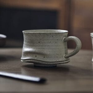 Side view of a Japanese Wabi-Sabi speckled pottery mug on a wooden table, highlighting the hand-pressed organic indentation near the base.