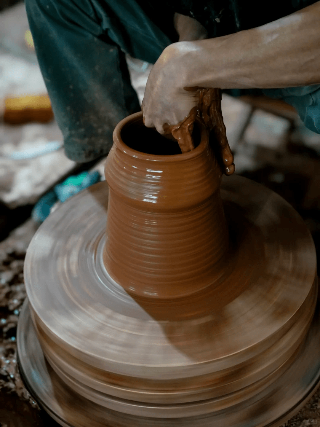 Close-up of a potter's hands shaping rich brown clay on a spinning wheel.