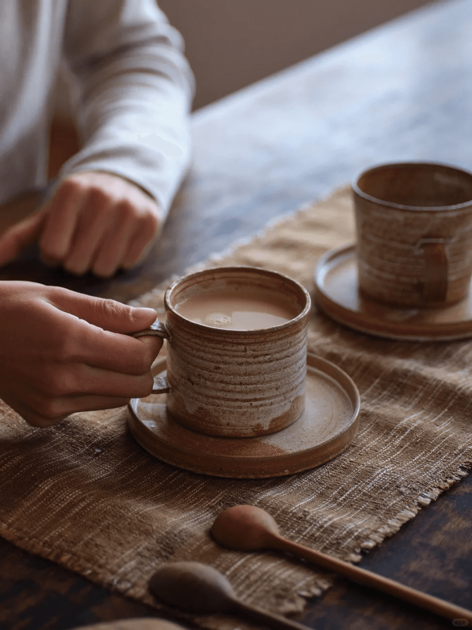 Cozy morning coffee routine featuring a handcrafted wabi-sabi ceramic mug with saucer on a linen mat.