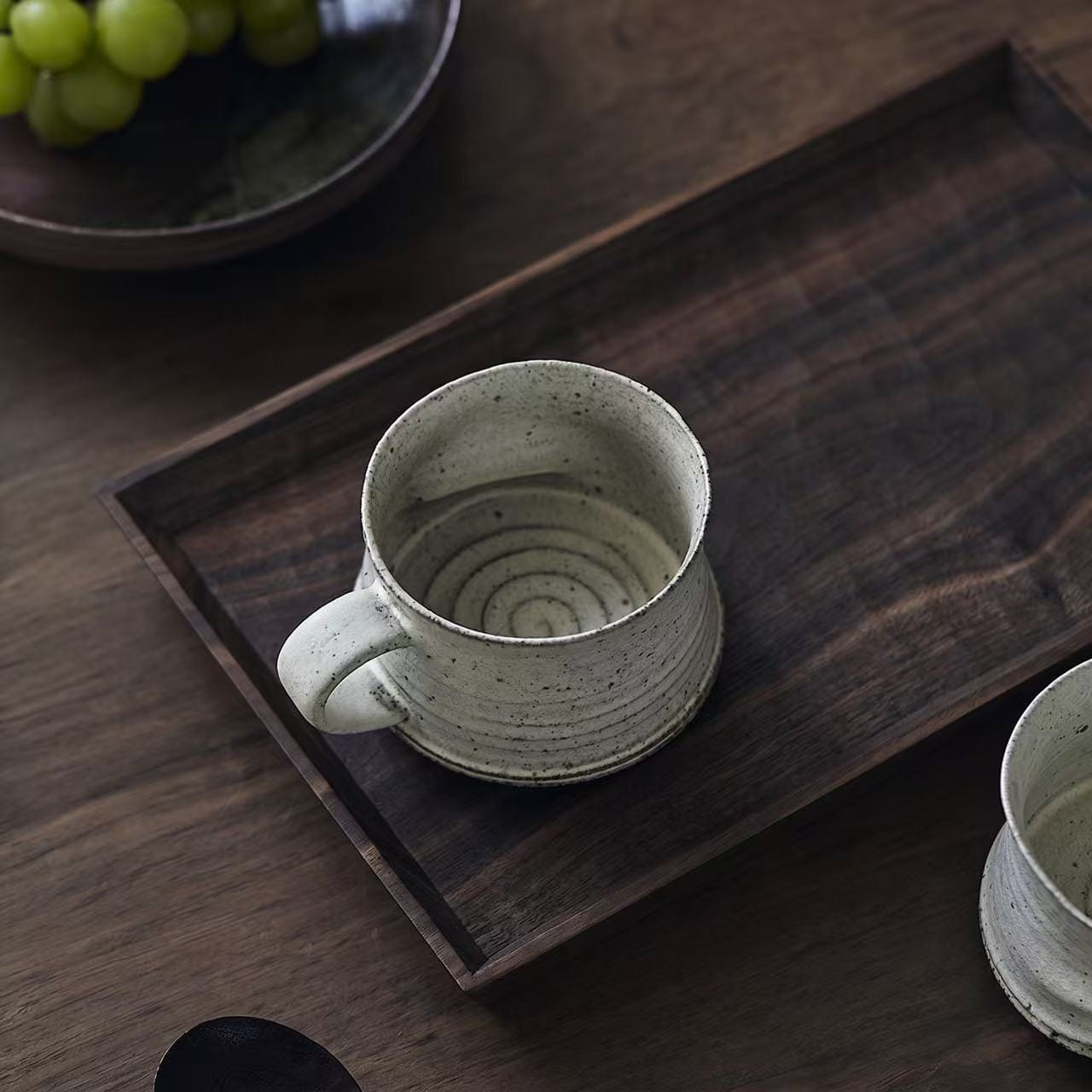 A rustic speckled ceramic mug with a unique texture resting on a dark wooden tray.
